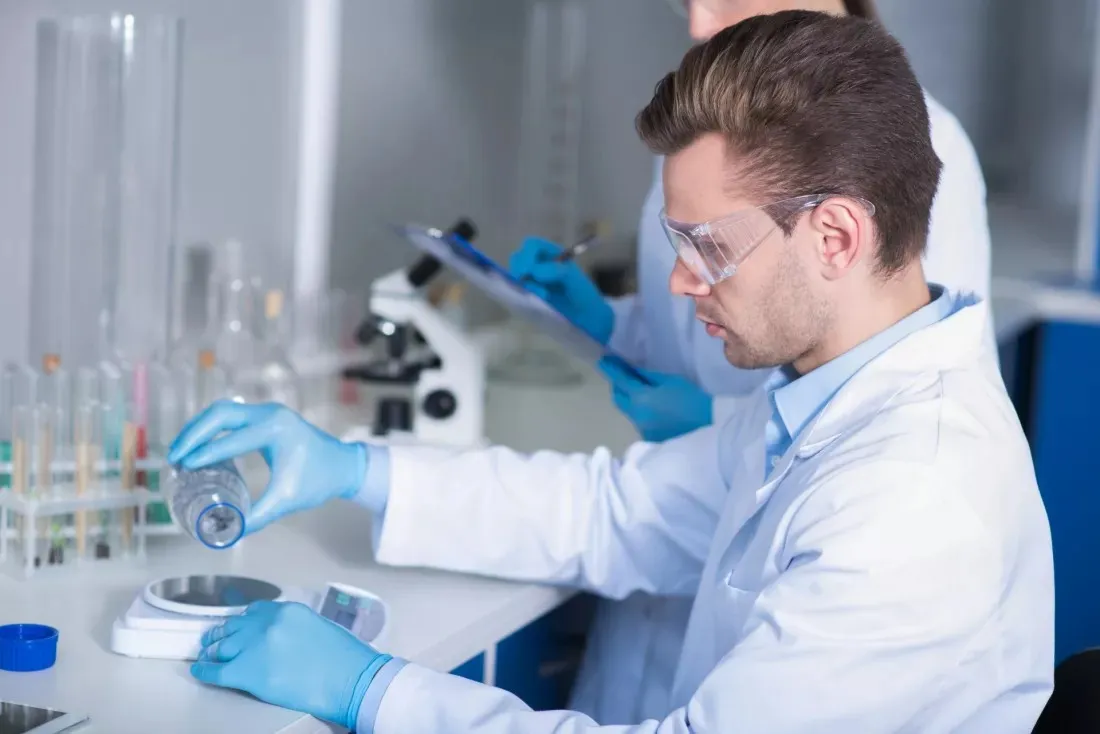 Junger Forscher mit Schutzbrille wiegt Substanzen auf einer Laborwaage ab