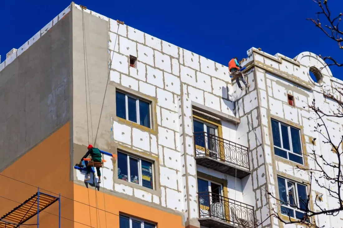 Bauarbeiter daemmen die Fassade eines aelteren Wohnblocks