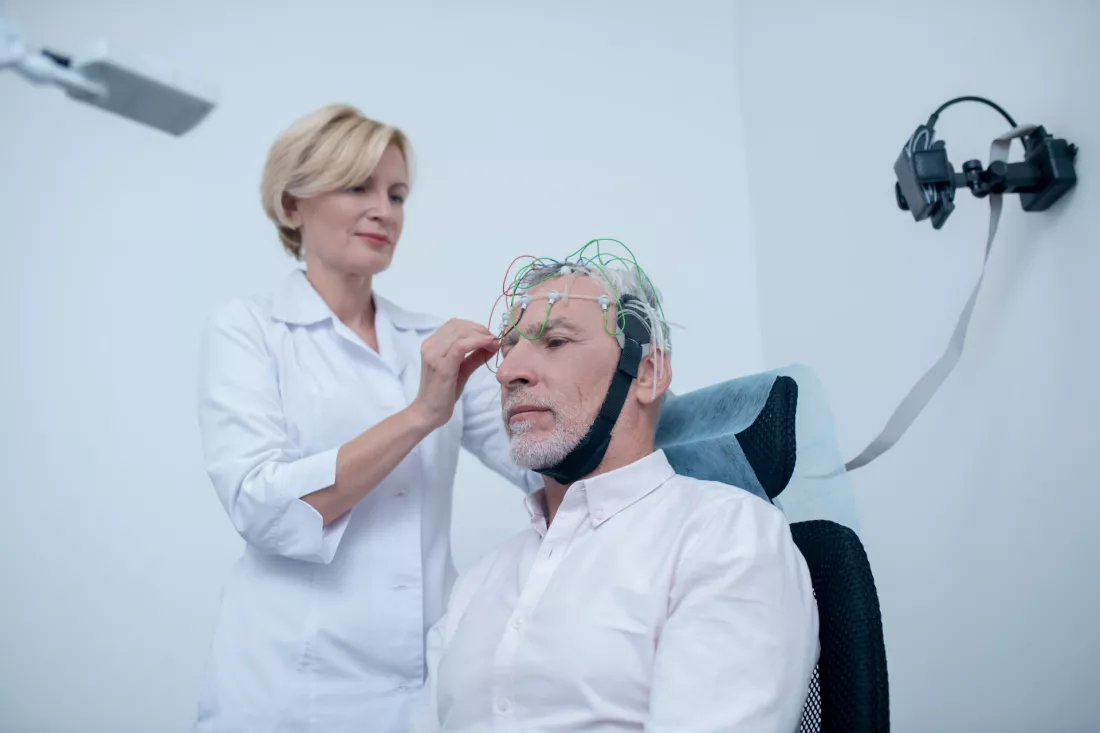 Eine Neurologin setzt einem aelteren Patienten eine EEG-Elektrodenhaube auf