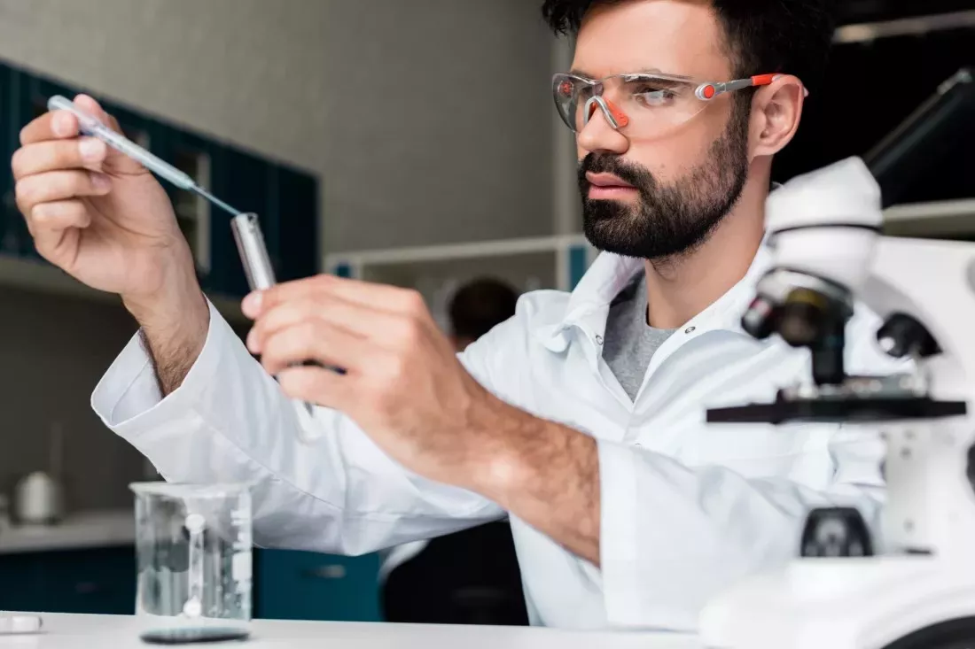 Forscher mit Schutzbrille fuellt mit einer Pipette eine Probe in ein Reagenzglas im Chemielabor