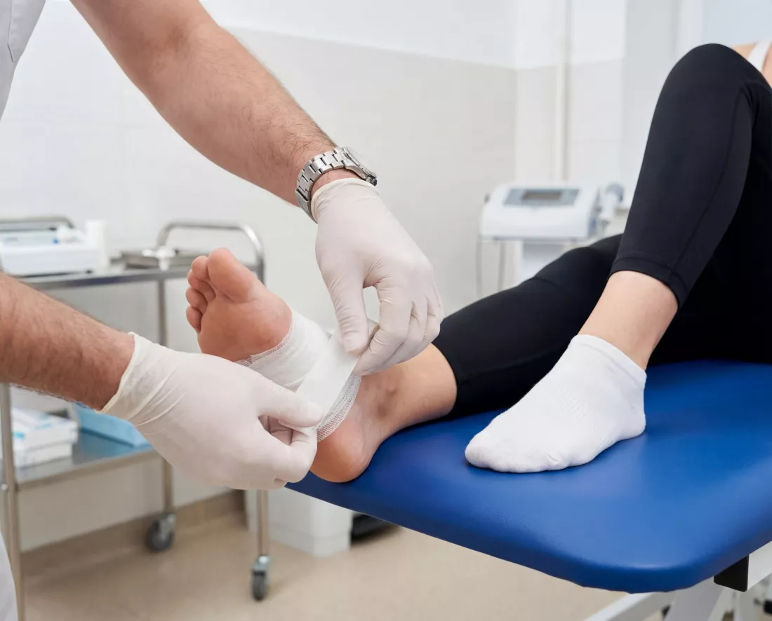 Arzt verbindet den Fuss einer Patientin in der Praxis