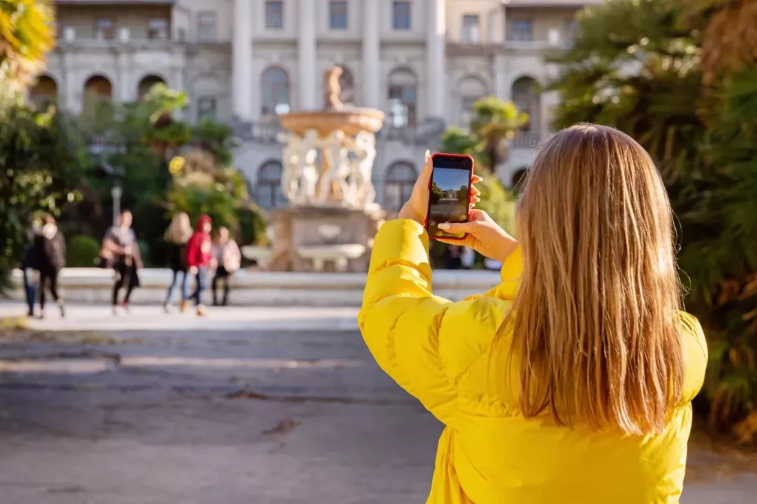 Junge Frau in gelber Jacke fotografiert einen Stadtplatz mit dem Handy