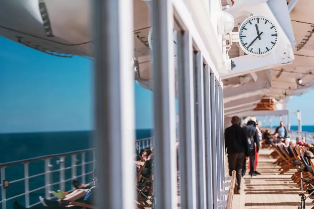 Passagiere gehen ueber das sonnige Deck eines Kreuzfahrtschiffs auf See